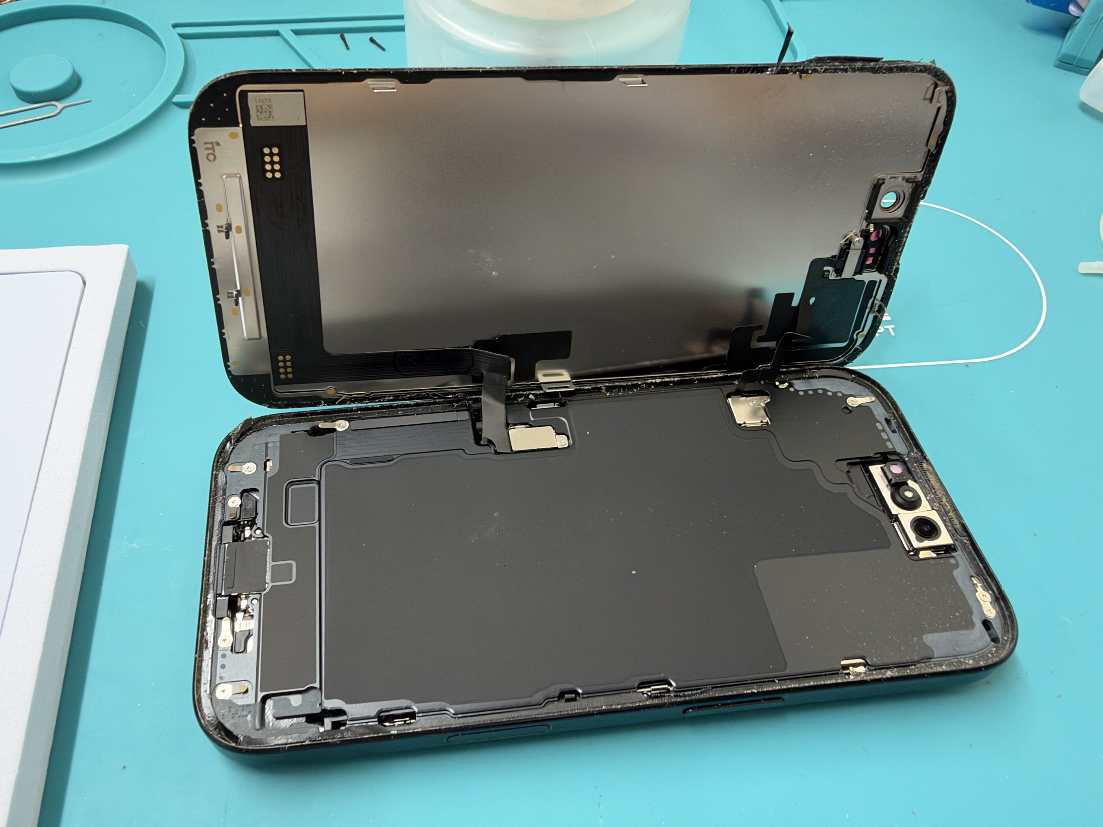 iPhone 16の画面を開き、破損した画面を取り外している作業中の様子